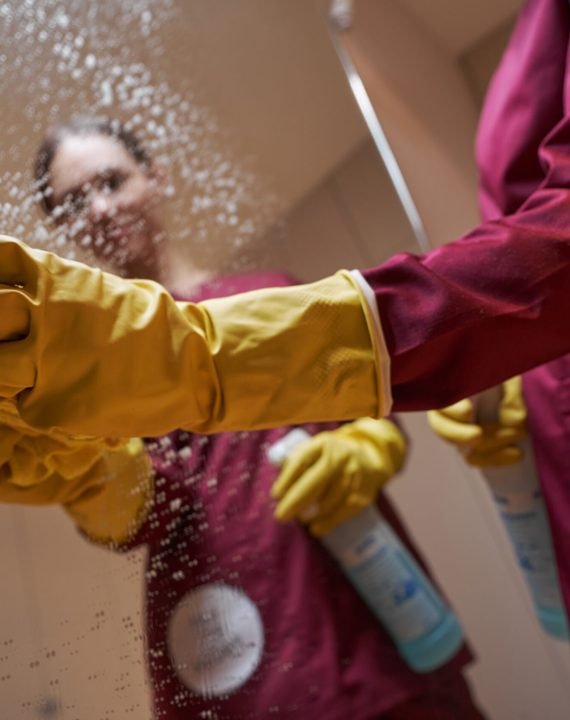 Dark-haired professional female cleaner removing drops of cleaning solution from mirrored surface